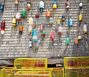 Lobster buoys hanging on the wall of a building with yellow lobster pots on the ground