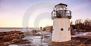 Lobster point lighthouse along the rocky coast of Maine at sunset on the Marginal Way path in Ogunquit during winter photo