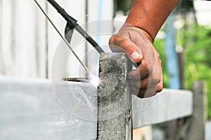 Local Asian technical worker welding steel iron on a concrete roof post in the outdoor day light construction work site.