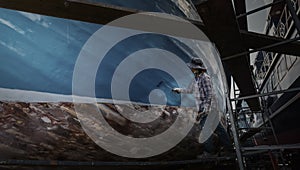 Local Asian woman painting on the side of a boat in shipyard for maintenance.