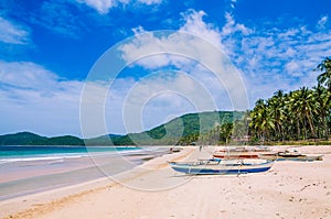 Local boats on wide Nacpan Beach on sunny day. El Nido, Palawan, Philippines