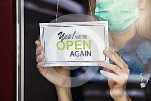 Local business owner with face mask turning open sign on shop door window