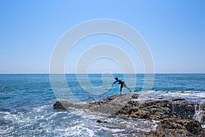 A local fisher man casting his fishing rod on rocks sea coast, shore of the Bay in Asia, Thailand