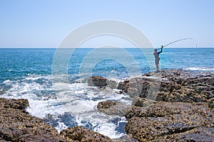 A local fisher man casting his fishing rod on rocks sea coast, shore of the Bay in Asia, Thailand
