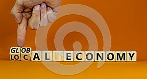 Local or global economy symbol. Businessman turns wooden cubes and changes words local economy to global economy. Beautiful orange