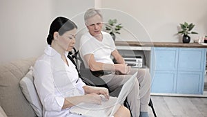 In a Local Hospital a Nurse Looks After a Gray Haired Man in a Wheelchair.