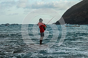 A local man in catches fish in the ocean on a sunny day to cook it for lunch. Indonesian man in red hoodie catches fish