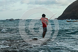 A local man in catches fish in the ocean on a sunny day to cook it for lunch. Indonesian man in red hoodie catches fish