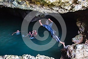 Local Polynesian teens playing and swimming in Veimumuni cave, while a girl jumping to the pool. Motion blur. Vavau, Tonga.