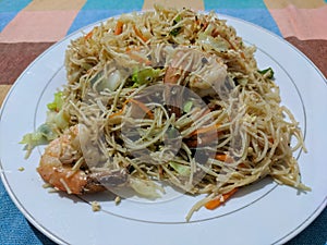 Local Sri Lanka dish. Noodles with vegetables and shrimp on a white plate in a cafe. Hikkaduwa, Sri Lanka