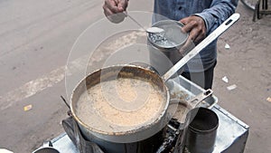 A local tea seller in a blue shirt adding a spoonful of sugar to freshly made tea - Indian Chai