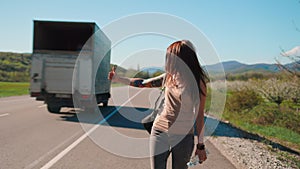 Local travel. Happy caucasian woman wearing glasses with tattoo hitchhiking with thumbs up in a countryside road waiting for a car