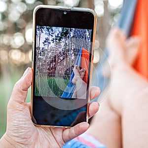 Local vacation. Woman having rest in hammock in the forest and making selfie