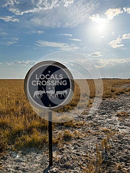 Locals crossing joke road sign in African savannah. Desert landscape.
