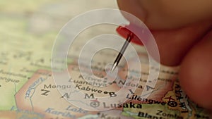 Location Zambia, Africa on travel map, man hand push pin close-up