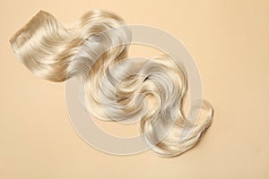 Lock of blonde wavy hair on color background