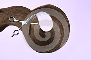 Lock of brown straight hair and thinning scissors on color background