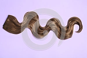 Lock of brown wavy hair on color background