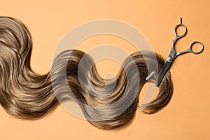 Lock of brown wavy hair and thinning scissors on color background