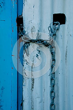 Lock and chain on a white corrugated iron wall with a blue door