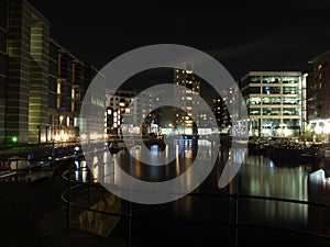 the lock entrance and moorings at clarence dock in leeds at night with buildings of the development reflected in the water and