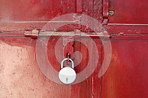 A lock placed on the red colored iron gate. Locked entrance of the warehouse during Covid-19 lockdown.