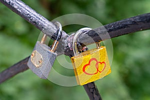 The lock, a symbol of love and loyalty, hangs on iron bars. Red Hearts are painted on a yellow lock. A piece of iron tree with