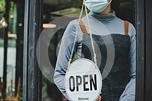 Lockdown. waitress staff woman wearing protection face mask turning OPEN sign board on glass door in modern cafe