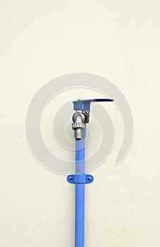 Locked faucet with blue PVC pipe on concrete wall