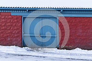 Locked gate of old wooden shed, red bricks with blue door in win