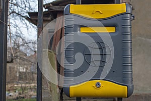 Locked plastic dark gray and yellow mailbox with globe symbol on it, with white envelope inside.
