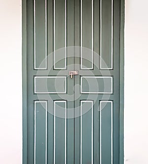 Locking green wooden vintage door in Thailand with cement white creamy colour wall beside it