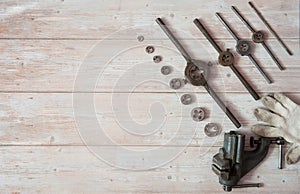 Locksmith vises, dies of different diameters and work gloves on a wooden background.