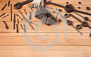 Locksmith vises, dies and taps of different diameters, a	pipe wrench and work gloves on a wooden background.