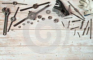 Locksmith vises, dies and taps of different diameters, a pipe wrench and work gloves on a wooden background.