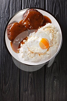 Loco Moco is Hawaiian comfort food made with rice and a burger smothered with rich gravy and egg close-up on a plate. Vertical top