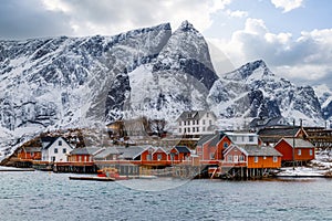 Lofoten islands, Norway, fishing village with red rorbu huts, snowy mountains in the background.