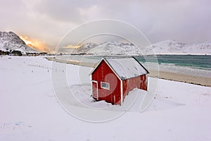 Lofoten Islands in Norway and their beautiful winter scenery at sunset. Idyllic landscape with red house on snow covered beach. To