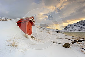 Lofoten Islands in Norway and their beautiful winter scenery at sunset. Idyllic landscape with red house on snow covered beach. To