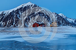 Lofoten islands, Norway. Typical houses of the fishermen rorbu, on the snowy beach, mountains in background.