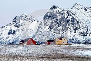 Lofoten islands, Norway. Typical houses of the fishermen rorbu, on the snowy beach, mountains in background.