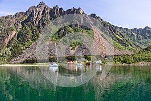 In the Lofoten Islands, sailboats drift by a remote farmstead with its characteristic red Rorbu