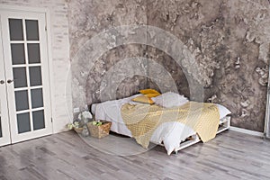 A loft style bedroom with recycled pallet bed. White and yellow bedding on bed with bedhead in loft bedroom interior