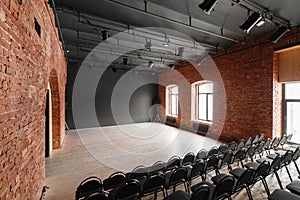 Loft style. Hall with black chairs for webinars and conferences. A huge room with large Windows, surrounded by brickwork