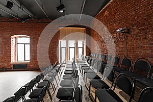 Loft style. Hall with black chairs for webinars and conferences. A huge room with large Windows, surrounded by brickwork