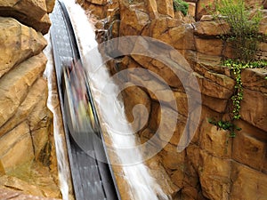 Log flume ride steep drop into artificial canyon with waterfall speed blur