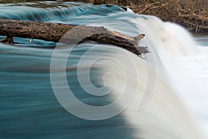 Log on top of waterfall resisting flow of river photo
