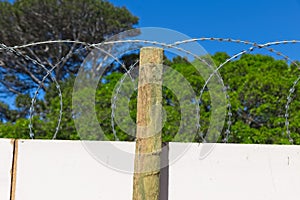 Log of wood against a wall with barbed wires on top of it with the trees in the background