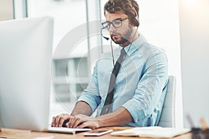 Logged in to listen. Shot of a young man working in a call center.