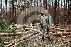 Logging, Worker in a protective suit with a chainsaw. Cutting down trees, forest destruction. The concept of industrial